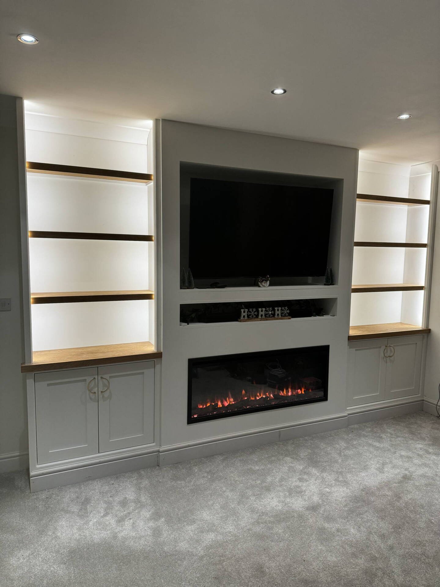 Painted media wall with built-in electric fire, TV recess and lit oak shelves